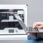 A designer works from a laptop with a 3D printer