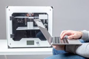A designer works from a laptop with a 3D printer